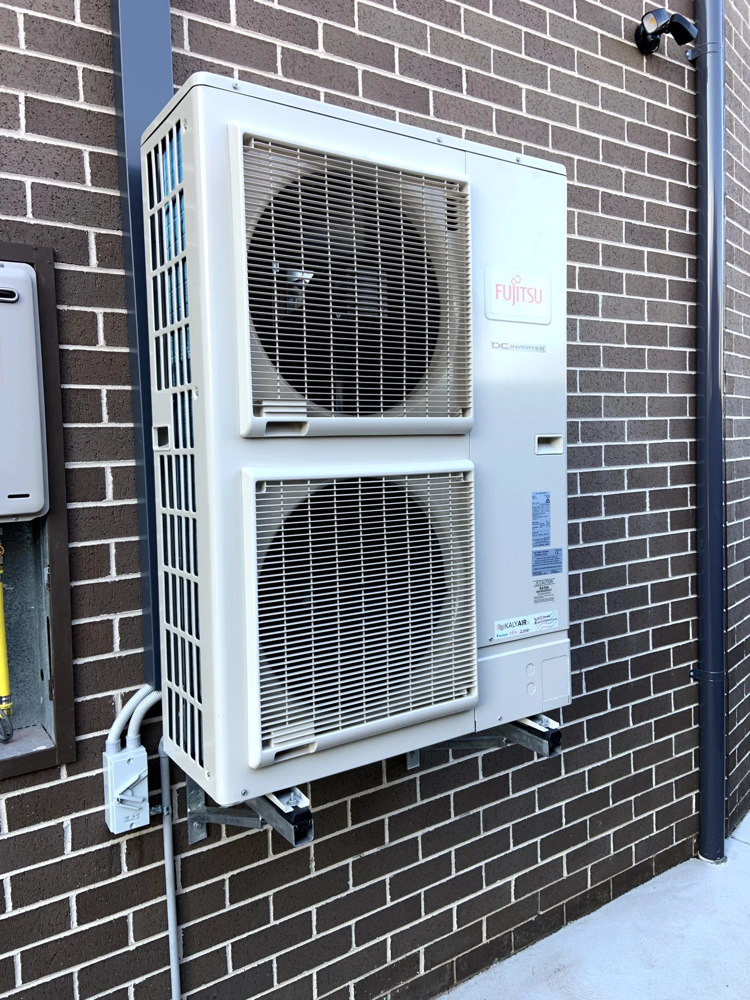 Outdoor twin-fan air conditioning unit mounted beside a brick home