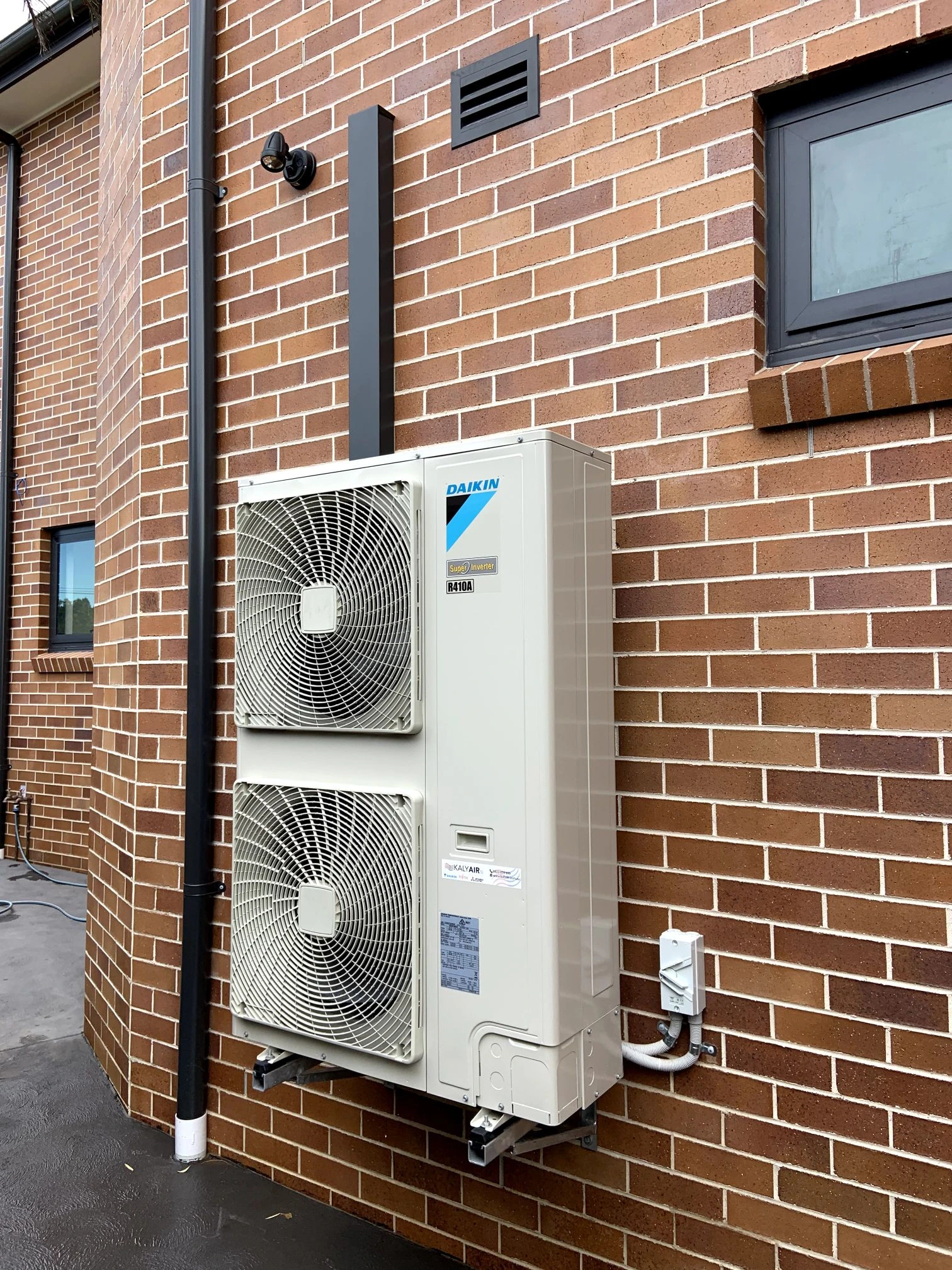 Twin-fan outdoor condenser mounted on a brick exterior wall